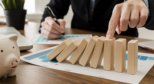 Businessperson preventing wooden domino blocks from falling, representing risk management, financial stability, and proactive decision-making in business strategy.
