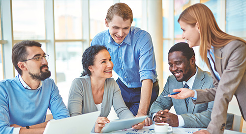Diverse business team gathered around a laptop discussing strategy in a bright modern office.