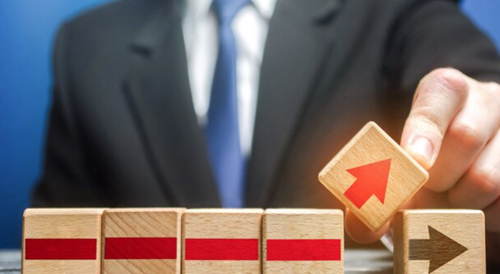 Businessman placing an upward arrow block among wooden direction blocks symbolizing growth and progress.