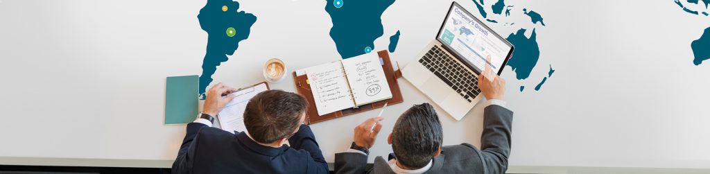 Business team reviewing expansion plans with a laptop and documents on a world map table.