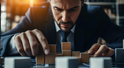 Focused businessman strategically arranging wooden blocks on a table, symbolizing business planning, risk management, and strategic decision-making in startups.