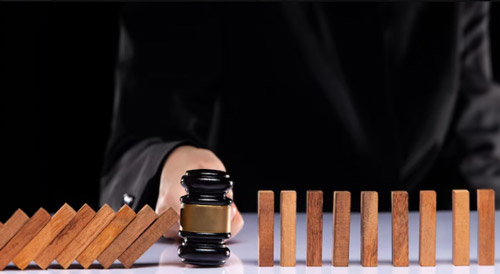 Person stopping falling wooden dominoes with a gavel in front, symbolizing risk prevention, legal protection, and crisis management in business or startups.